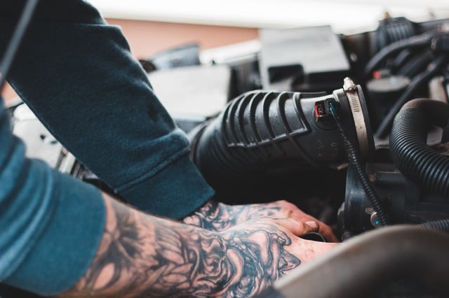 Tattooed mechanic's arm reaching into an engine bay