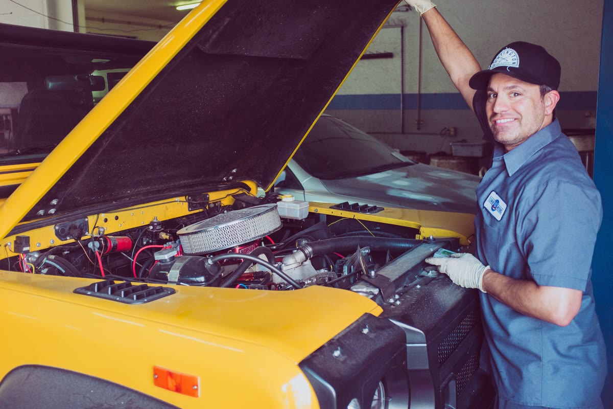 Smiling mechanic in uniform beside a yellow car with its hood open